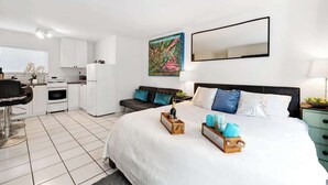 A modern hotel room with a large bed, a sitting area with a sofa and a dining table, a kitchenette, and a bathroom. - MB Studio with Parking Sleeps 4 Steps to Sand (San Diego)