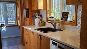 Una cocina moderna con armarios de madera, lavavajillas de acero inoxidable y un ventanal con un cartel de bienvenida.