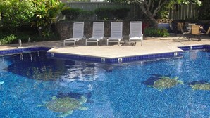 A clear blue pool with four lounge chairs and a small table, surrounded by greenery.