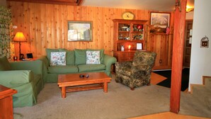 Una sala acogedora con un sofá verde, una mesa de centro de madera y un sillón camuflado.