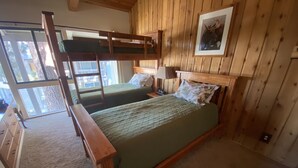 Habitación con literas, cabecera de madera, mesita de noche con lámpara y un cuadro en la pared.