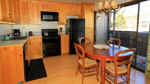 Una cocina con armarios de madera, un refrigerador negro, una estufa y una mesa de comedor con sillas.