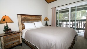 Una cama grande con cabecera de madera, dos mesitas de noche con lámparas, y vistas a muebles de exterior a través de una puerta de cristal.