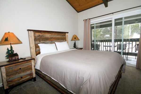 A large bed with a wooden headboard, two bedside tables with lamps, and a view of outdoor furniture through a glass door.