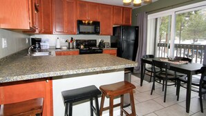 Una cocina con armarios de madera, encimera de granito, microondas, refrigerador y un comedor con mesa y sillas.