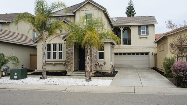 A two-story house with a stone facade, a garage, and a front yard with palm trees and a small garden. - Modern Living, relax and enjoy your stay! (Rancho cordova)
