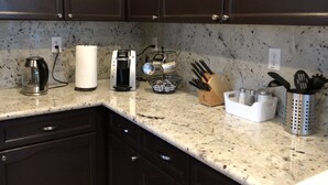 A kitchen with dark cabinets, a coffee maker, a kettle, a paper towel holder, a knife block, and a spice rack. - Modern Living, relax and enjoy your stay! (Rancho cordova)