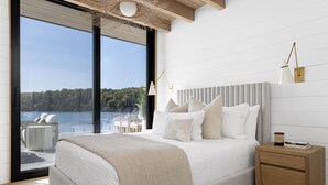 Un dormitorio con una cama grande, una mesita de noche, una lámpara y vistas a un lago.