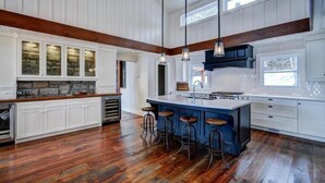 Une cuisine spacieuse avec des meubles blancs, un grand îlot central doté de tabourets et un pare-feu en pierre.