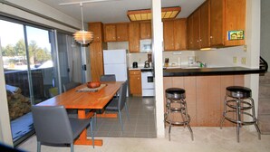 A modern kitchen with wooden cabinets, a central island with stools, a dining table with chairs, and a large window. - Sierra Park Villas #24 (Mammoth Lakes)