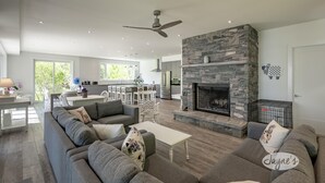 A spacious living room with a gray sectional sofa, a fireplace, and a modern kitchen in the background.