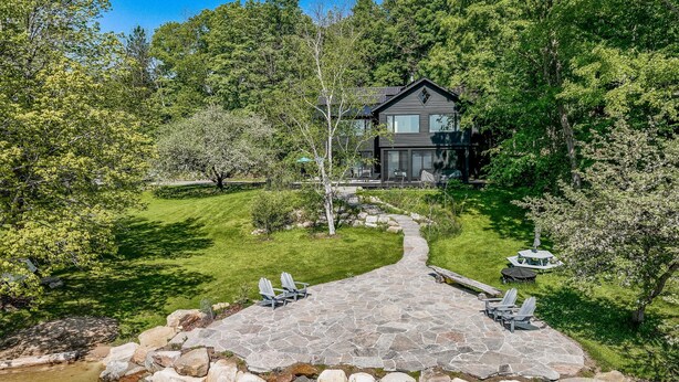 A stone pathway leading to a house surrounded by lush greenery and a small stream.