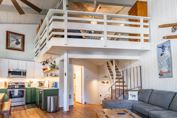 A spacious living area with a loft bedroom, wooden floors, a kitchen with modern appliances, and a staircase. - Sierra Park Villas #04 (Mammoth Lakes)