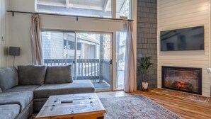 A modern living room with a sectional sofa, a wooden coffee table, a fireplace, and a large sliding glass door leading to a balcony. - Sierra Park Villas #04 (Mammoth Lakes)