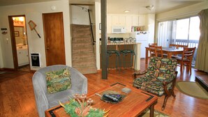 A living room with a grey sofa, a patterned armchair, a wooden coffee table, and a staircase leading to a kitchen. - Sierra Park Villas #16 (Mammoth Lakes)