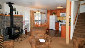 A living room with a fireplace, a dining area, and a kitchen with wooden cabinets and a microwave. - Sierra Park Villas #29 (Mammoth Lakes)