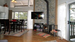 A modern living room with a stone fireplace, a flat-screen TV, and a dining area with wooden chairs and a table. - Sierra Park Villas #03 (Mammoth Lakes)