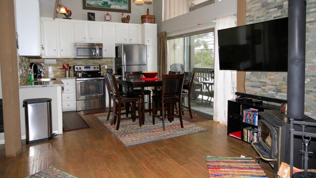 A kitchen with white cabinets, a microwave, a stove, and a dining area with a table and chairs. - Sierra Park Villas #03 (Mammoth Lakes)