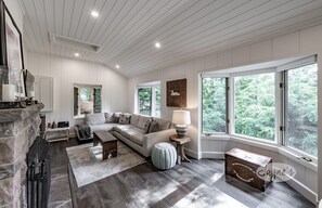 Relax in this stylish living room with a large sofa, side table, and stone fireplace, offering a view of the surrounding greenery.