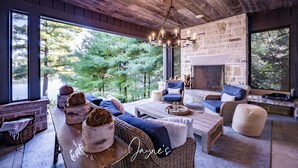 A cozy room with wicker furniture, a stone fireplace, and large windows overlooking a forest. - 5-year old, Luxury Build on Joe! Immaculate Main + Guest Cottage! Tennis! (Mactier)