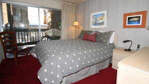 Une chambre avec un grand lit, une chaise, une table de chevet, une lampe et une fenêtre avec des rideaux.