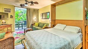 Habitación de hotel con cama, escritorio, silla, ventilador de techo y vista a zonas verdes.