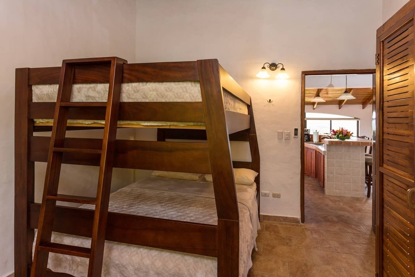 A bunk bed with a wooden ladder, a kitchenette in the background, and a wooden door.