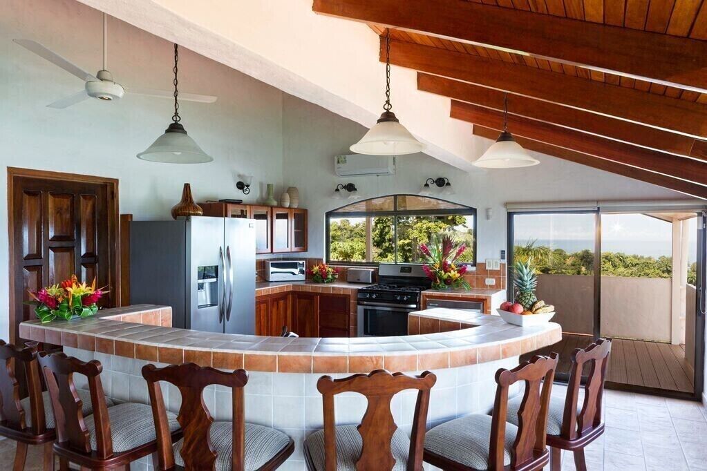 Een moderne keuken met een gebogen kookeiland, houten stoelen en uitzicht op de omgeving.