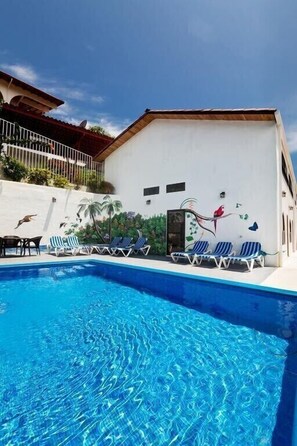 A swimming pool with lounge chairs and a mural of birds and palm trees on the building. - Casa Moreno - Spectacular Views, Close to Beaches, Marina, Tours, Shopping! (Manuel Antonio)