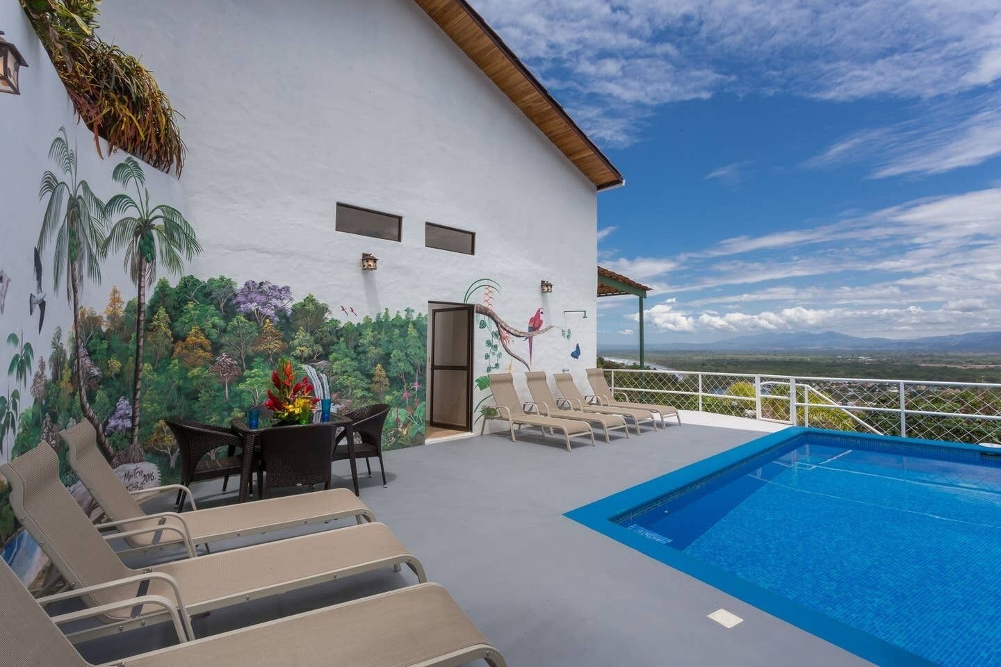 A rooftop pool area with lounge chairs and a mural of tropical scenery.
