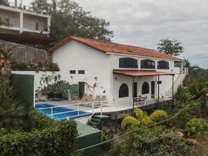 A two-story white building with a red-tiled roof, a swimming pool, and a balcony with outdoor seating. - Casa Moreno - Spectacular Views, Close to Beaches, Marina, Tours, Shopping! (Manuel Antonio)