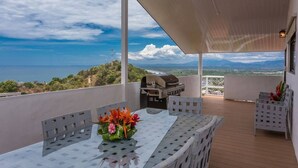 Un espace extérieur abrité, équipé d’une table et de chaises, d’un barbecue et offrant une vue sur le paysage.