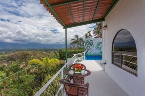 A balcony with a view of a lush landscape, a mural, and a table with flowers. - Casa Moreno - Spectacular Views, Close to Beaches, Marina, Tours, Shopping! (Manuel Antonio)