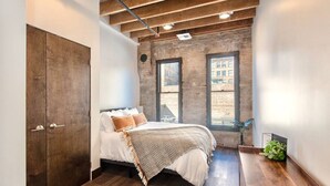 Une chambre à coucher avec un lit, une armoire en bois et une vue sur l’extérieur grâce à de grandes fenêtres.