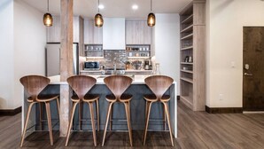 Une cuisine moderne dotée d’un îlot central, de tabourets de bar, de luminaires suspendus et de meubles de rangement en bois.