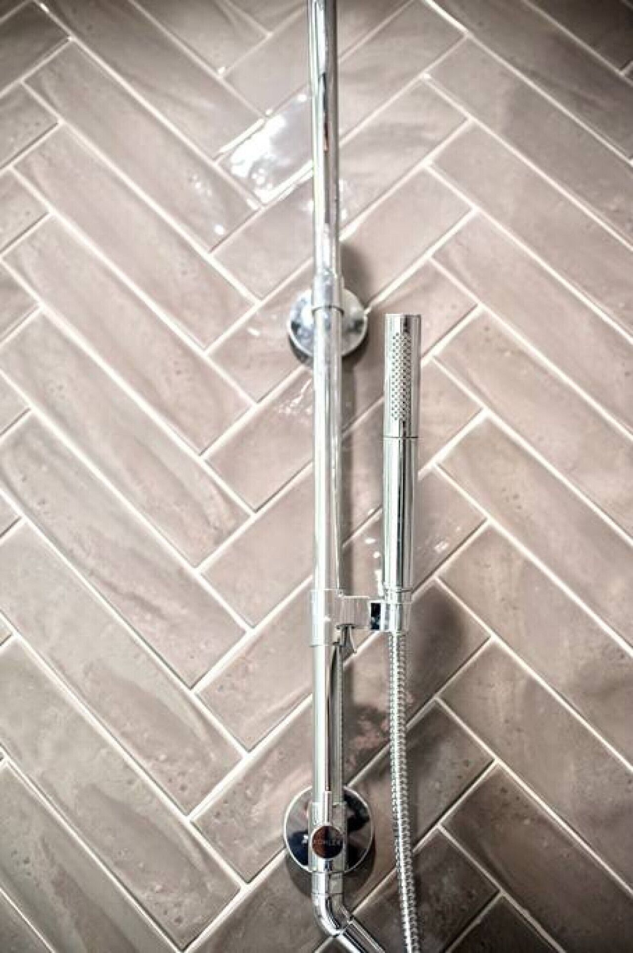 A shower with a chrome finish, mounted on a tiled floor with a herringbone pattern.