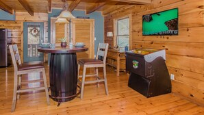 Un accogliente interno di una baita con arredamento in legno, un tavolo da calcio, una televisione e un'area pranzo con sedie e tavolo.