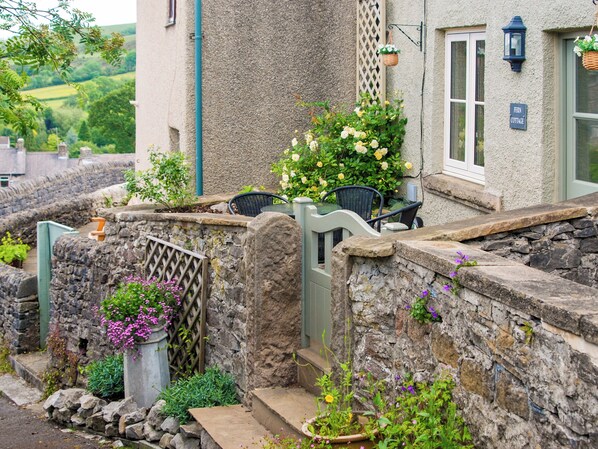 A stone wall with a small garden, a wicker chair, and a sign reading 'Fern Cottage.'