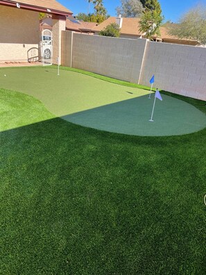 A backyard with artificial grass, a white gate, and a brick wall.