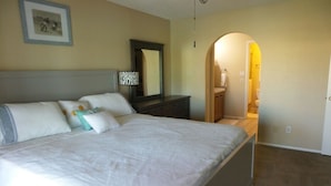 A bedroom with a large bed, a dresser, a mirror, and a bathroom visible through an archway. - WATER FRONT SWEET HOME (Mesa)