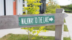 A wooden sign with a green background and white text that reads "WALKWAY TO THE LAKE" with an arrow pointing to the right. - Downtown Solar Home w/ Hot Tub & Billiards (Geneva)