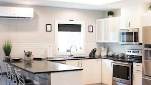 A modern kitchen with white cabinets, a stainless steel oven, a microwave, and a sink. - Downtown Solar Home w/ Hot Tub & Billiards (Geneva)
