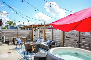 An outdoor patio area with a hot tub, wicker furniture, and string lights. - Downtown Solar Home w/ Hot Tub & Billiards (Geneva)