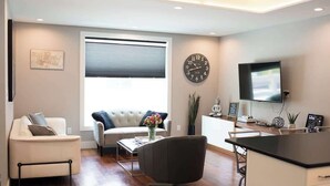 A modern living room with a sofa, armchair, coffee table, and a TV. - Downtown Solar Home w/ Hot Tub & Billiards (Geneva)