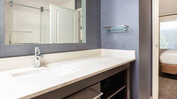 A modern bathroom with a large mirror, a white sink, and a glass shelf.