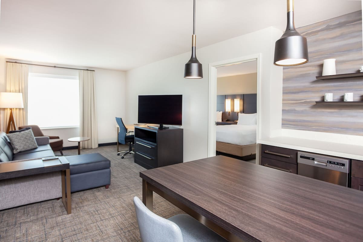 Ett modernt hotellrum med ett matbord i trä, en soffa, en TV, ett skrivbord och en diskmaskin.
