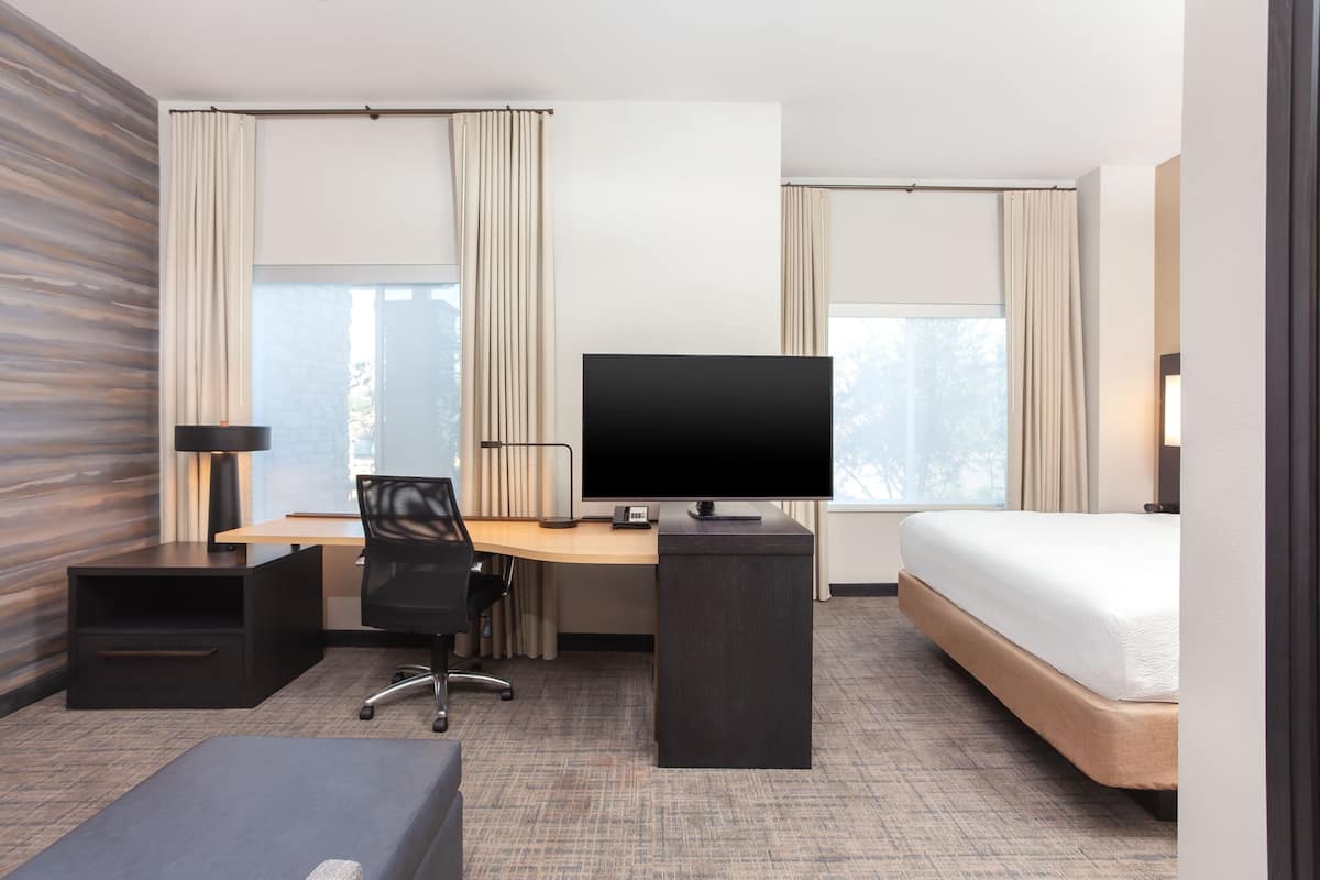 Ett modernt hotellrum med en stor säng, ett skrivbord med en dator, en stol och en TV.