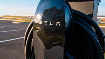 A Tesla charging station with a clear view of the charging cables and the Tesla logo.