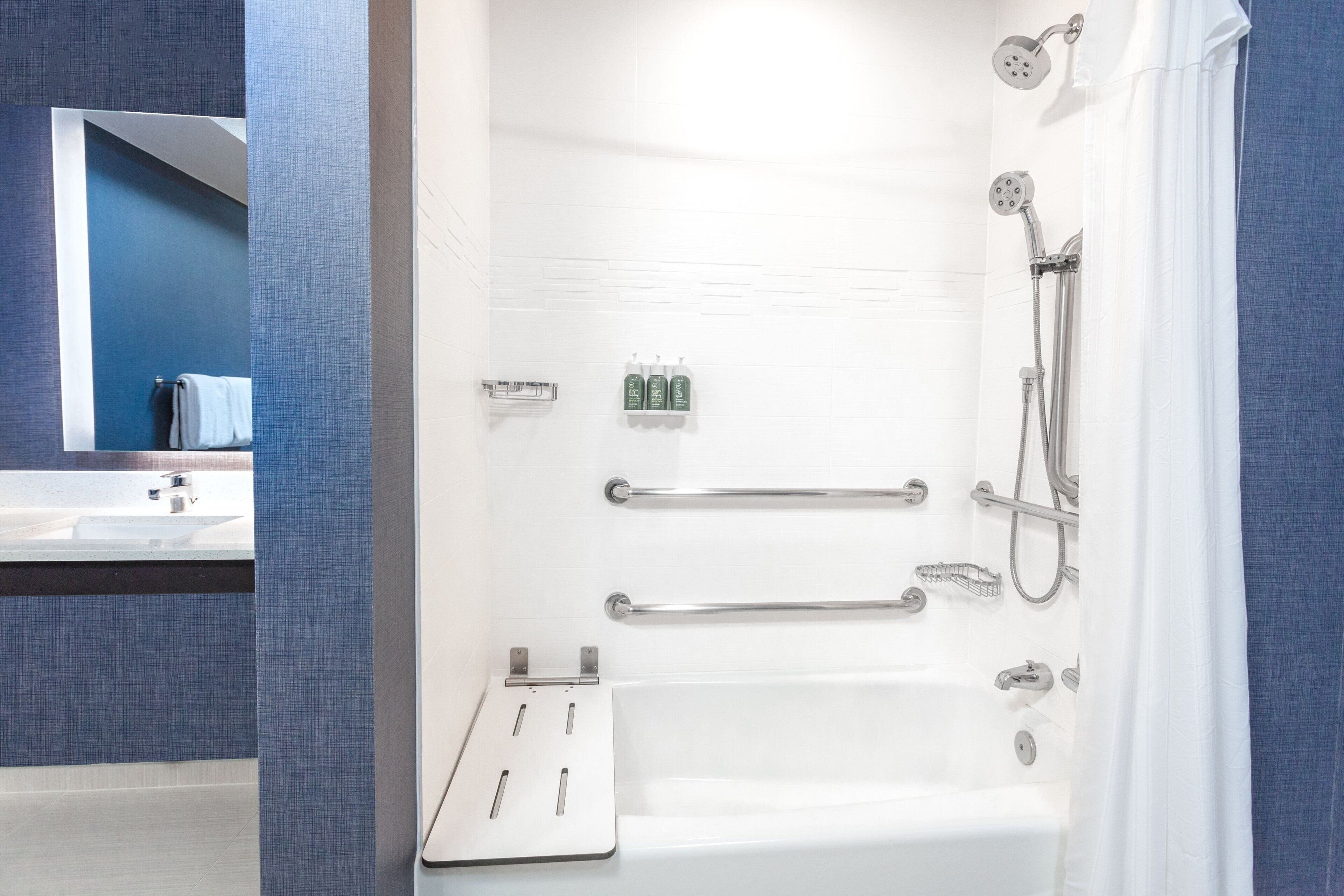 A modern bathroom with a bathtub, shower, and handrails.