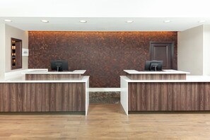 A reception area with two reception desks, a wooden textured wall, and a door. - Residence Inn by Marriott Livermore (Livermore)